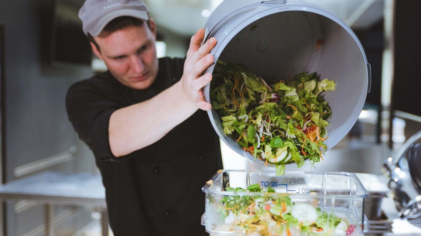 Ein Mitarbeiter wirft Salat aus einem großen Eimer zum Wiegen in die Abfalltonne