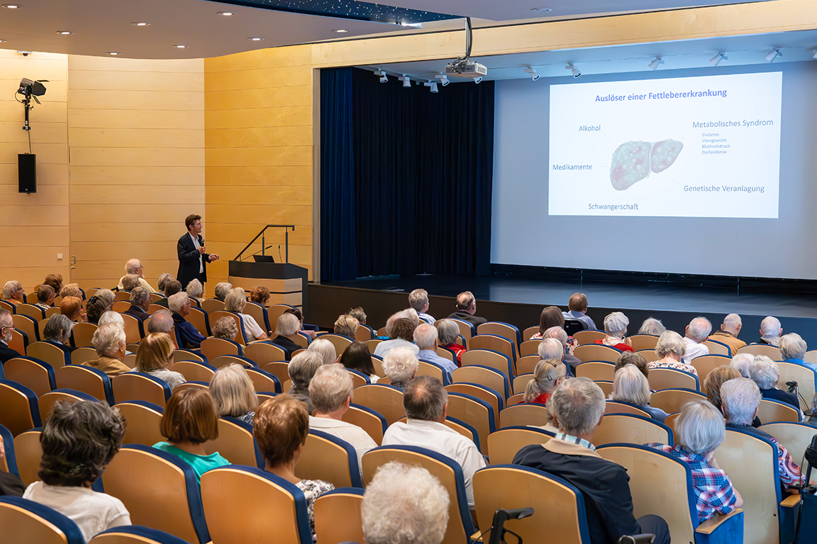 Dr. Tilman Gerlach hält seinen Vortrag zum Thema Fettlebererkrankung vor den im Theatersaal versammelten Senior*innen
