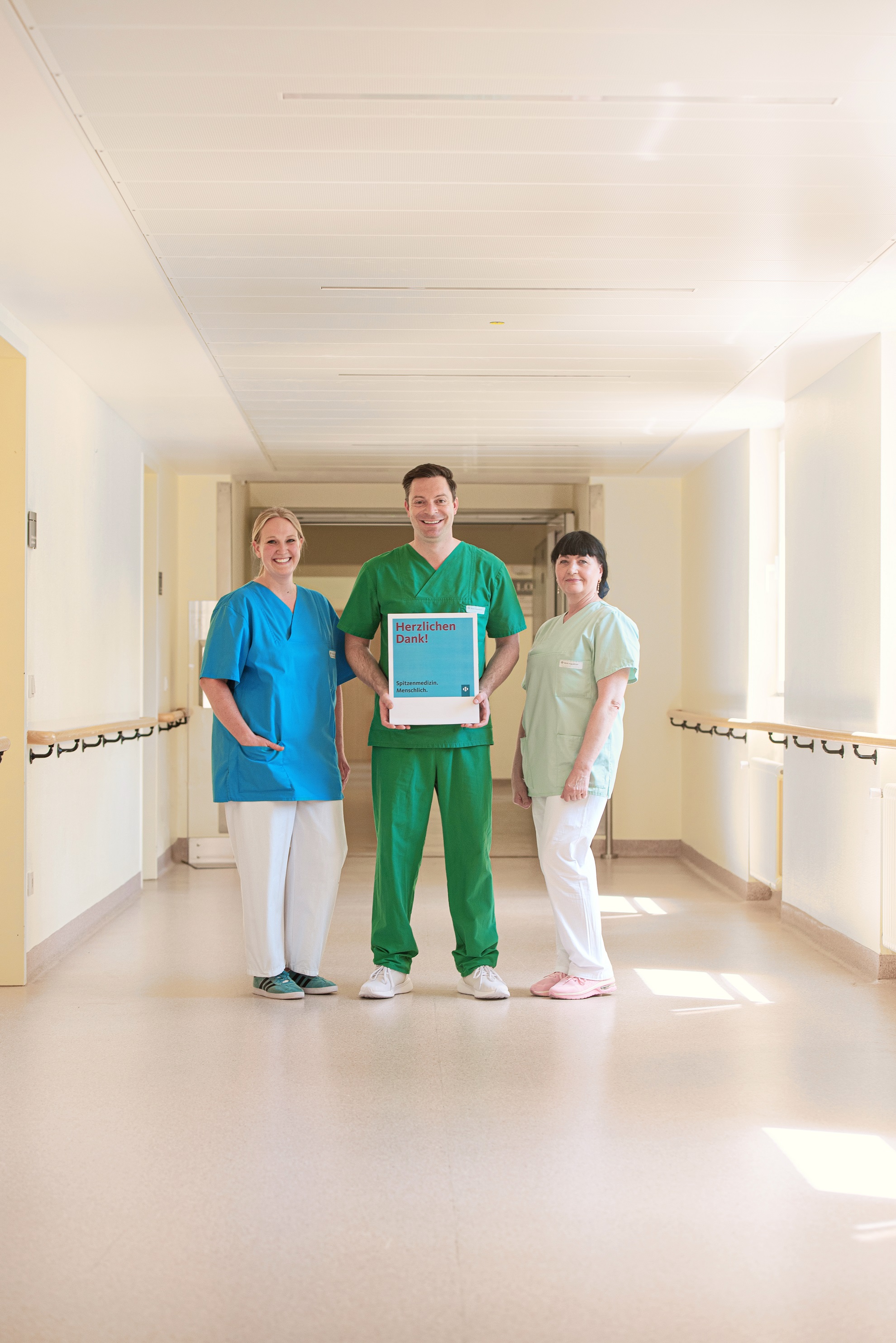 Augustinum Klinik München Danke Drei Mitarbeiter*innen der Augustinum Klinik halten ein Schild mit der Aufschrift "Herzlichen Dank"