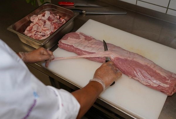Ein*e Koch*Köchin pariert ein großes Stück Fleisch