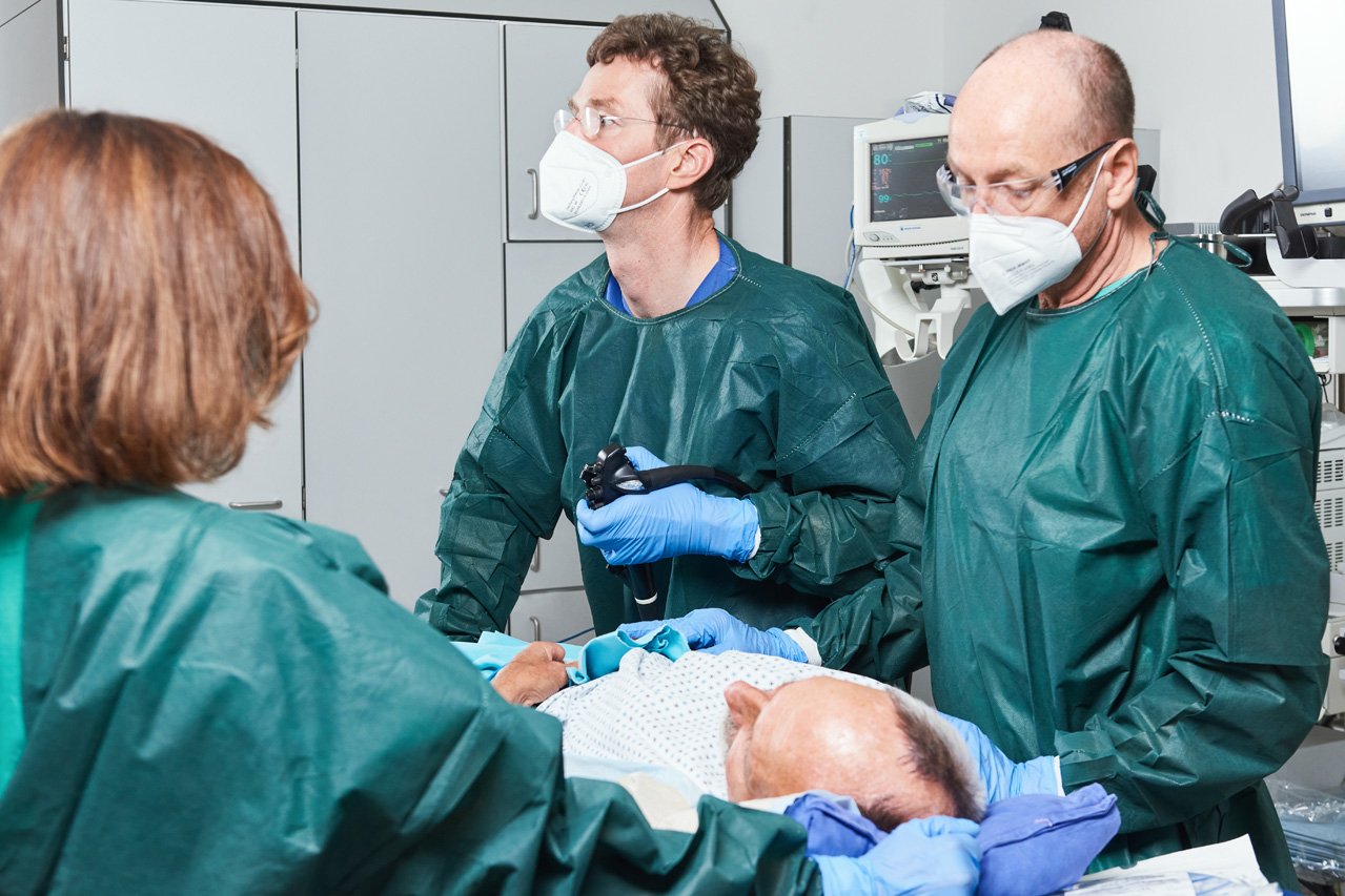 Ein dreiköpfiges Behandlungsteam steht um einen liegenden Patienten, bei dem eine Magenspiegelung durchgeführt wird.