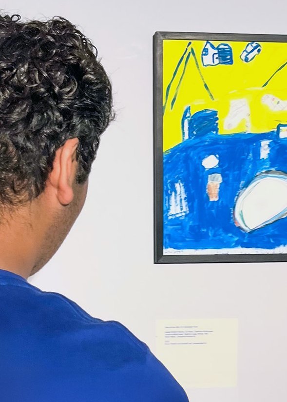 ein junger Mensch schaut sich ein buntes Bild in einer Ausstellung an