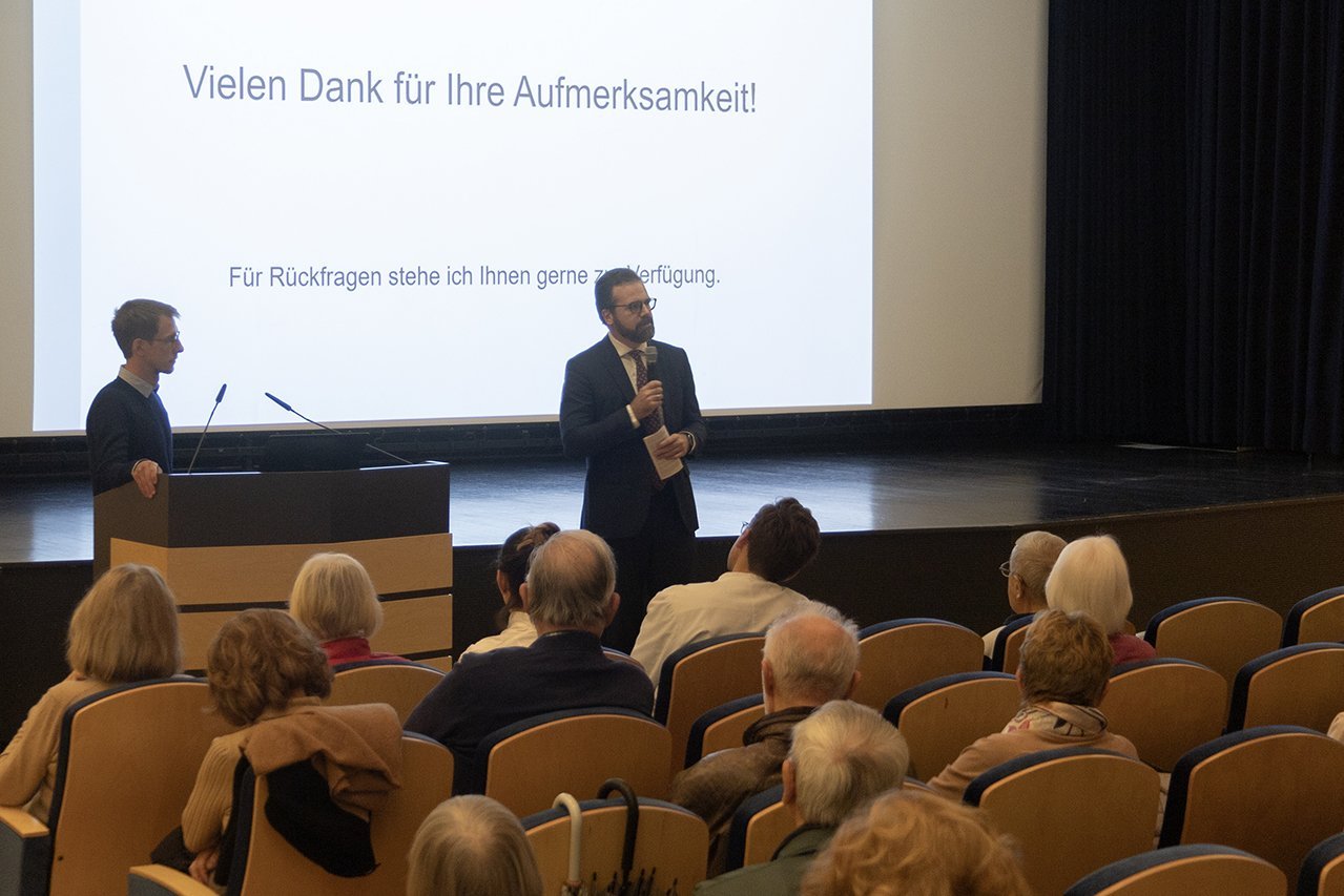 Dr. Friedel und Dr. Husser stehen vor dem Publikum und beantworten am Ende des Vortrags Rückfragen 