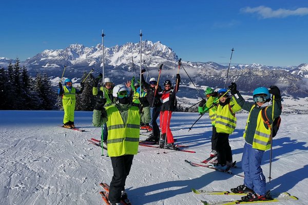 Ein Gruppenfoto von Schüler*innen beim Skifahren, wobei jeder seine/ihre Skistöcke in die Luft hebt