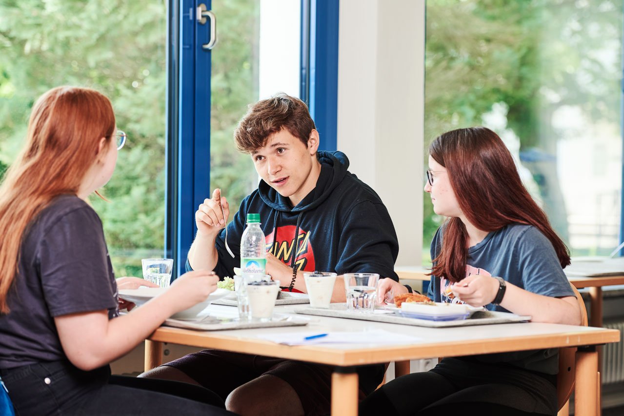 Schüler*innen sitzen an einem Tisch in der Mensa