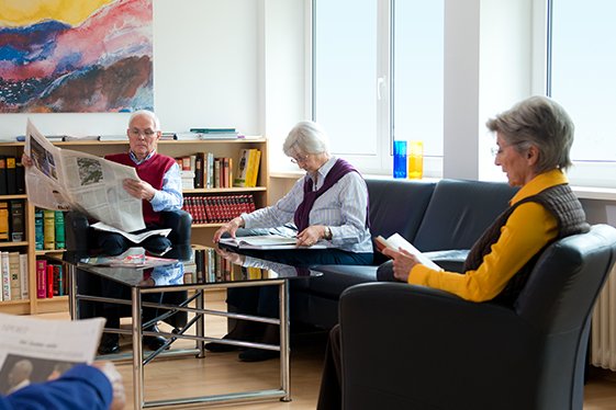 Vier Senior*innen lesen Zeitung in einem Gemeinschaftsraum