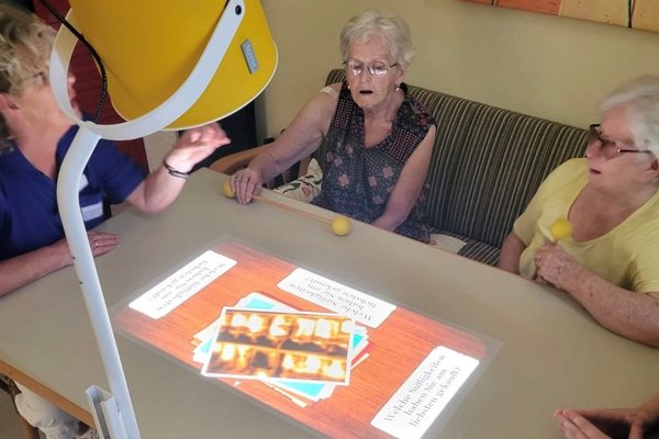Seniorinnen sitzen an einem Tisch, auf den ein Spiel mithilfe einer Tovertafel projiziert wurde