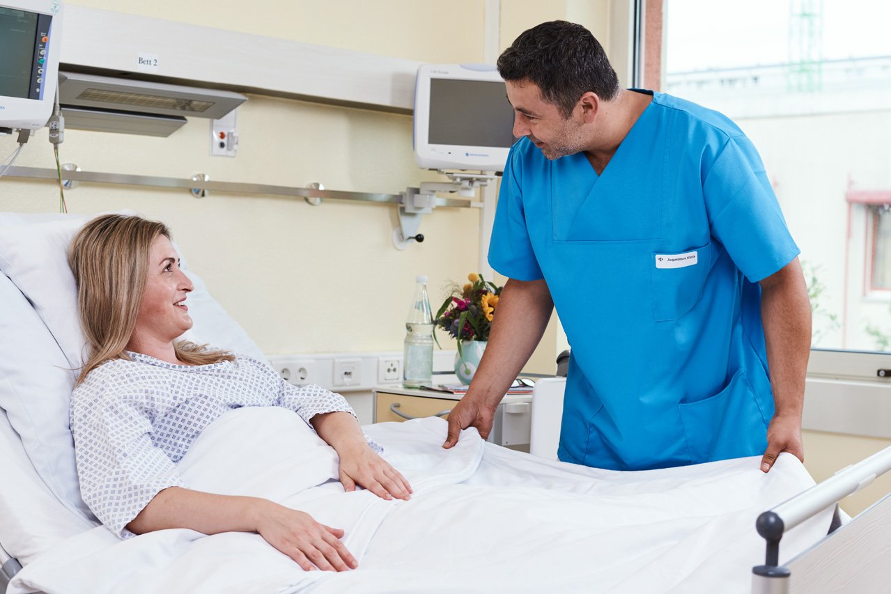 Das Bild eines Pflegers im Gespräch mit einer Patientin mit Link zur Fachabteilung Pflege und Betreuung der Augustinum Klinik