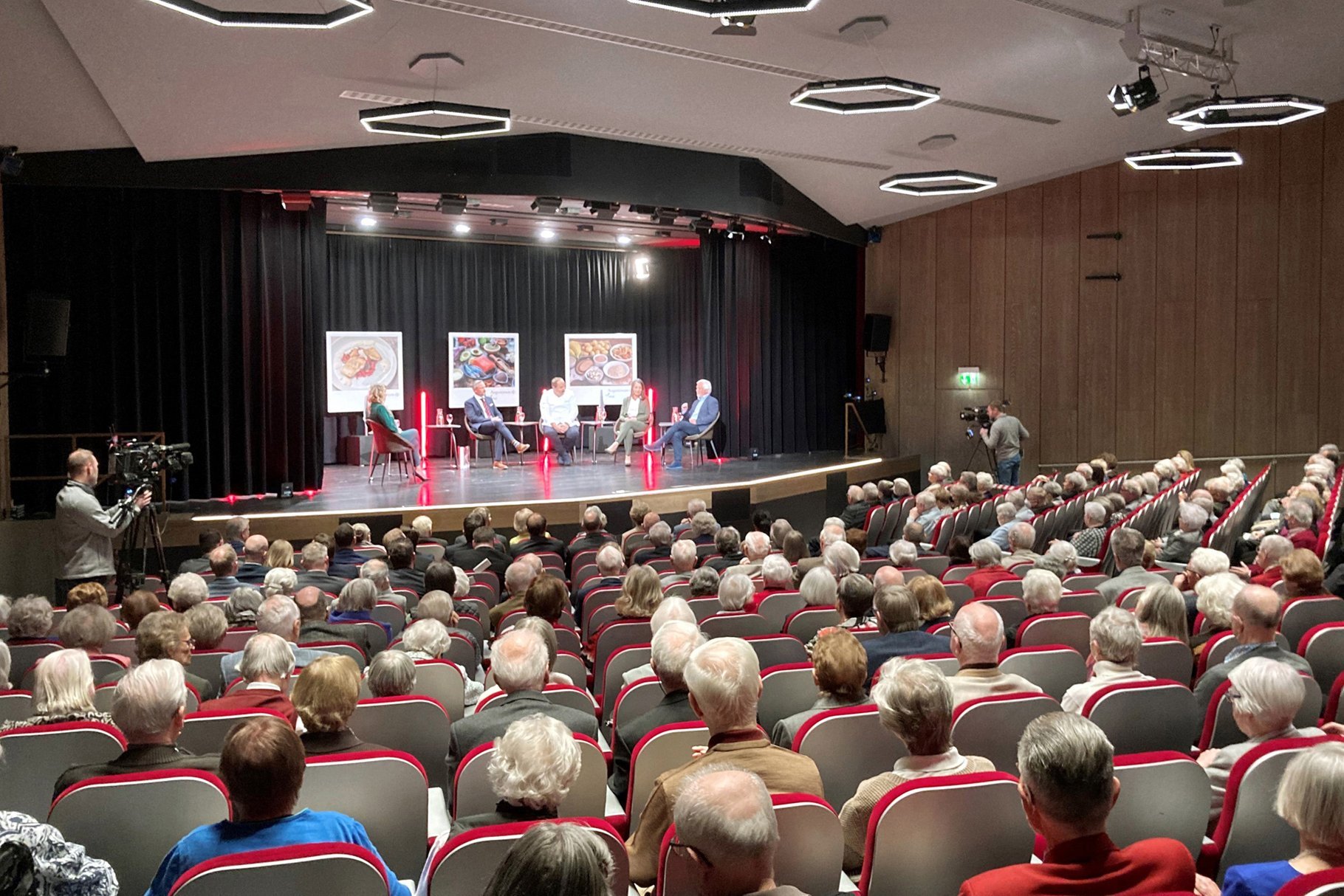 Senior*innen sitzen im Theatersaal während sich fünf Leute auf der Bühne unterhalten