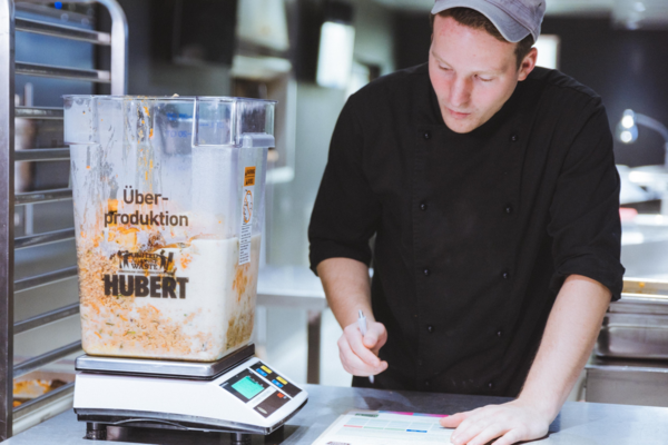 Ein Koch notiert das Gewicht eines Behälters mit Lebensmittelmüll