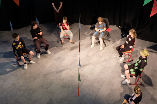 Augustinum Inklusive Theater AG Eine Aufnahme von oben zeigt Kinder, die in einem Theaterraum im Stuhlkreis sitzen, während die Lehrerin an der Seite steht