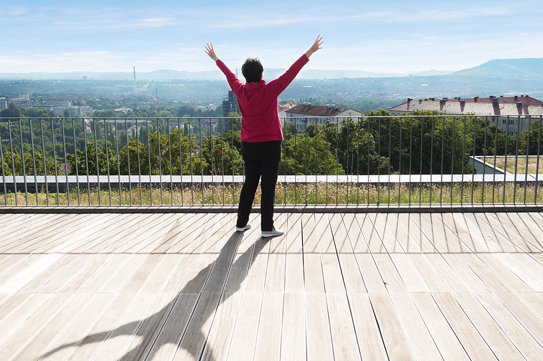 Dame mit ausgebreiteten Armen auf einer Dachterrasse