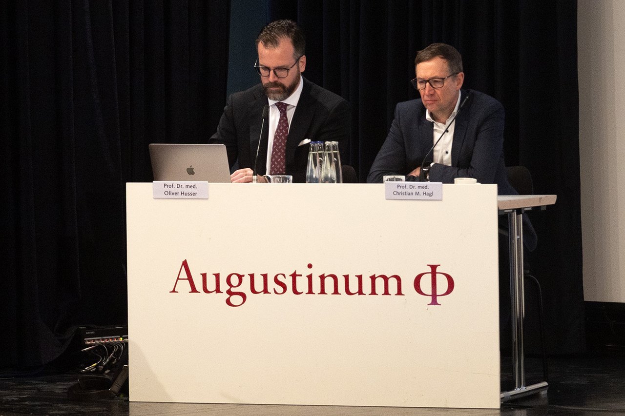Prof. Dr. Husser der Augustinum Klinik und Prof. Dr. Hagl des LMU Klinikum sitzen bei der Veranstaltung auf der Bühne