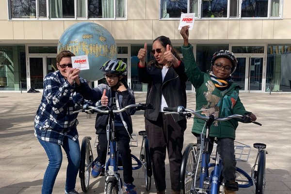 Ein Gruppenbild von zwei Schülern, die jeweils auf einem Dreirad sitzen, und zwei Erwachsenen vor der Otto-Steiner-Schule, die jeweils Daumen nach oben zeigen