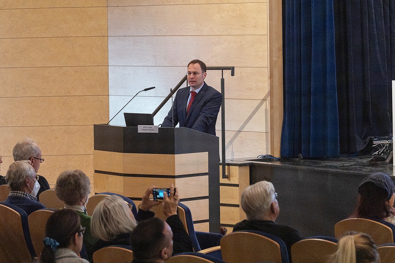 Dr. Patzelt von der Augustinum Klinik steht an einem Rednerpult vor dem Publikum während er seinen Vortrag hält 