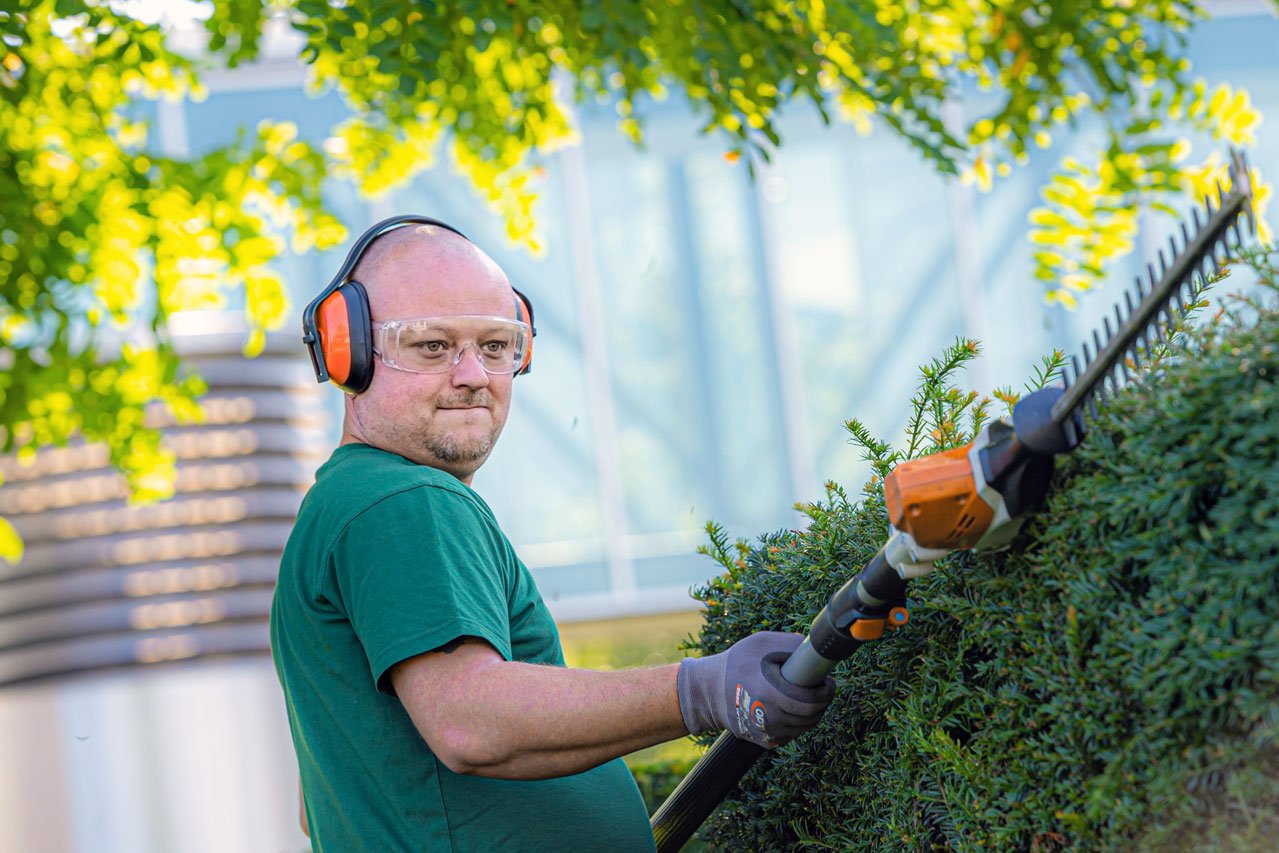 Ein Klient der Augustinum Gärtnerei Hollern schneidet mit einer akkubetriebenen Teleskopheckenschere die Hecke