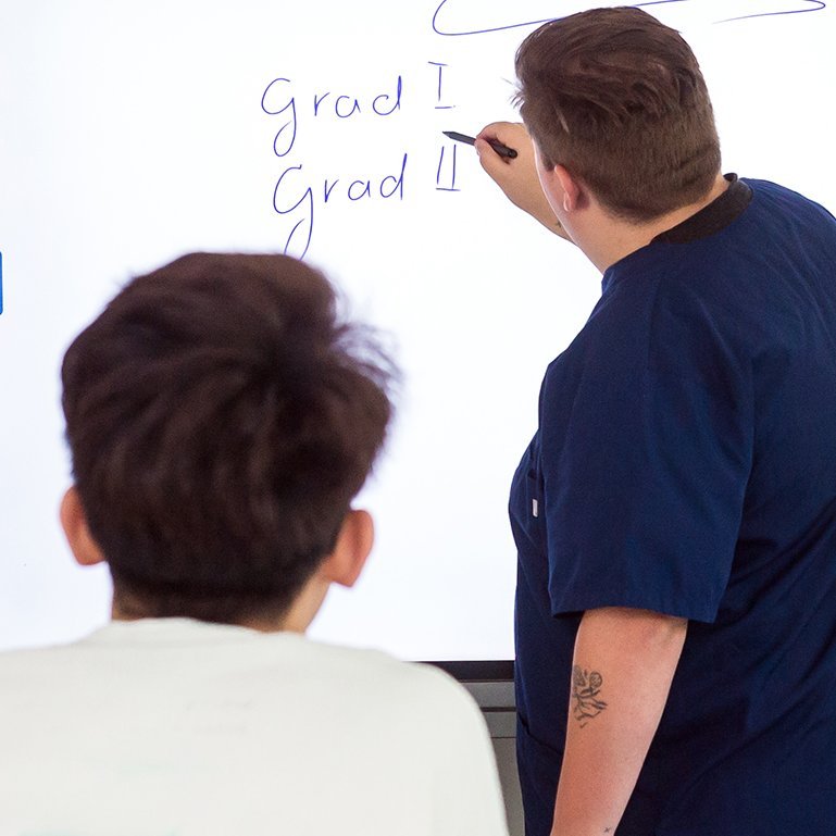 Ein Schüler schreibt bei einem Kurs der Berufsfachschule für Pflege etwas an die Tafel