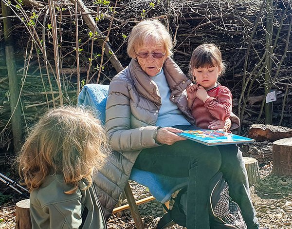 Seniorin ließt Kindergartenkindern aus einem Buch