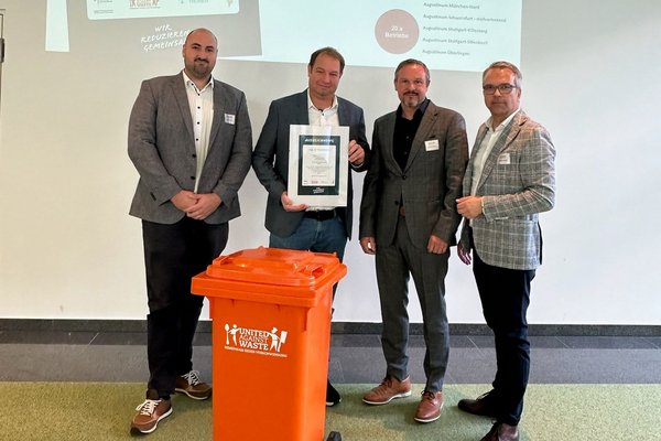 Die drei Projektbeteiligten des Augustinum zusammen mit dem Geschäftsführer von United against Waste halten die Urkunde für die Auszeichnungen in den Händen, im Vordergrund eine orangene Mülltonne