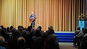 Die Musikerin Annett Kuhr sitzt vor einem Publikum auf der Bühne, spielt Gitarre und singt in ein Mikrofon 