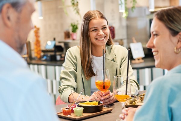 Drei Gäste sitzen an einem Tisch im Vierundsiebzig, unterhalten sich, lachen und trinken einen Spritz