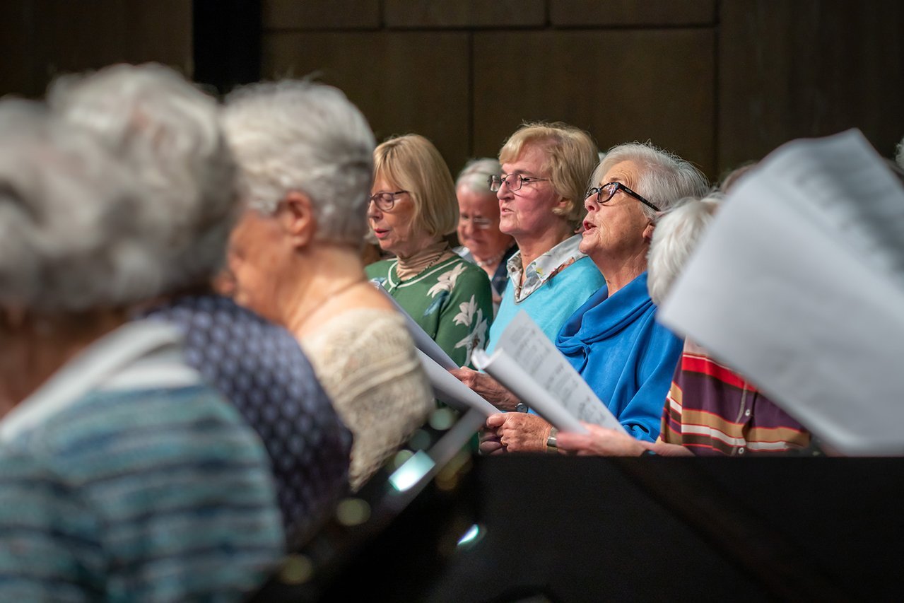 Seniorinnen sitzen in einem Saal und singen