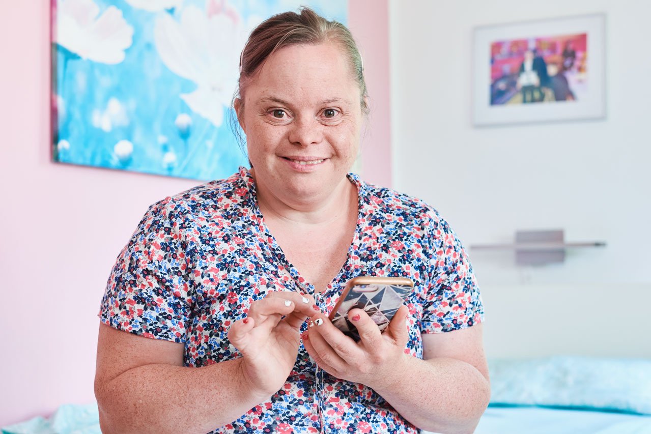Eine Frau mit einem Handy in der Hand sitzt auf einem Bett