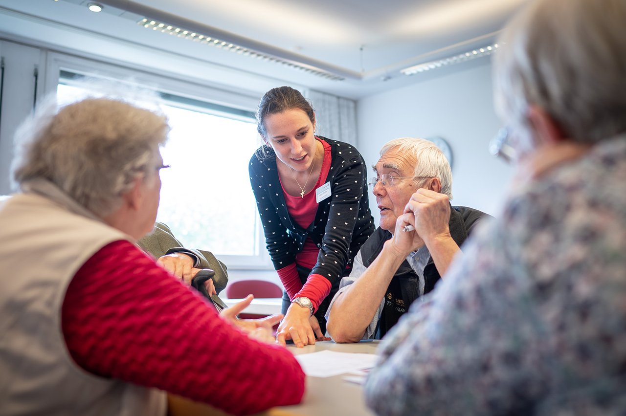 Eine Mitarbeiterin des Augustinum erklärt etwas den Senior*innen 
