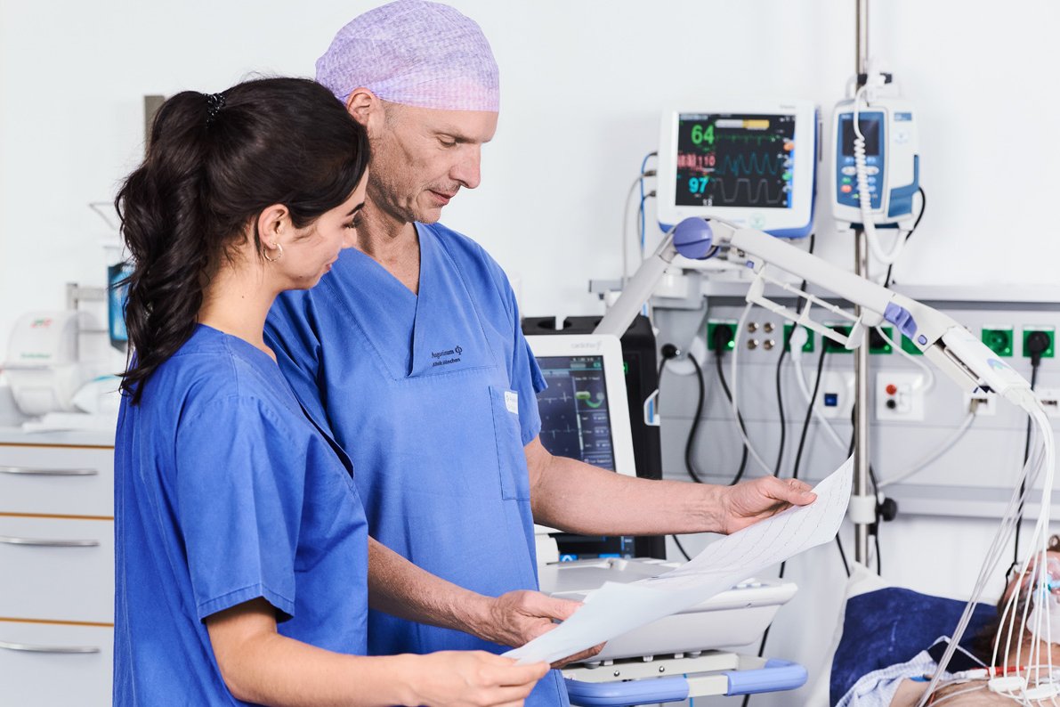 Bild eines Arztes und einer Pflegerin bei der Kontrolle des EKGs eines Patienten mit einem Link zur Chest Pain Unit der Augustinum Klinik