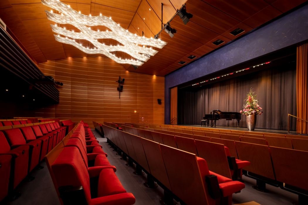 Ein Theatersaal mit roten Sitzen und einer Bühne, auf der ein Konzertflügel steht.