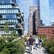 Menschen spazieren auf einem begrünten Fußweg zwischen modernen Hochhäusern und historischen Backsteingebäuden in im dicht bebauten New York.