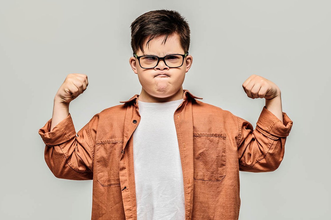 Kleiner Junge zeigt mit grimmigem Gesicht seine Muskeln
