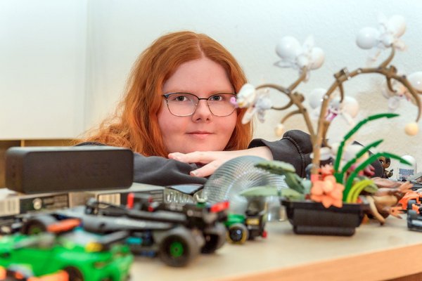 Das Mädchen steht hinter einem Regal, auf dem sich viele Deko-Artikel befinden, und blickt in die Kamera