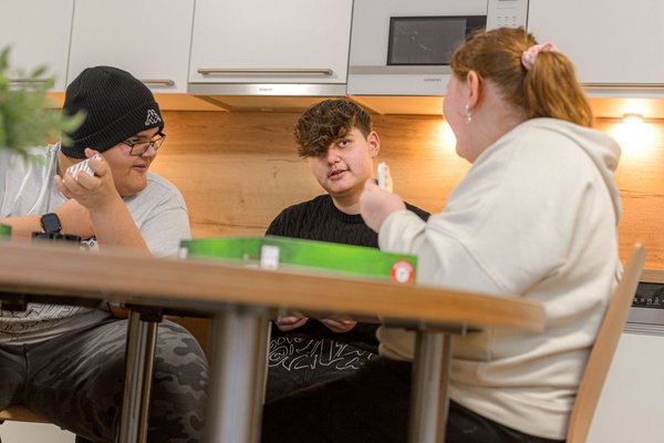 Drei Jugendliche der Adipositas Wohngruppen sitzen an einem Tisch und spielen ein Kartenspiel