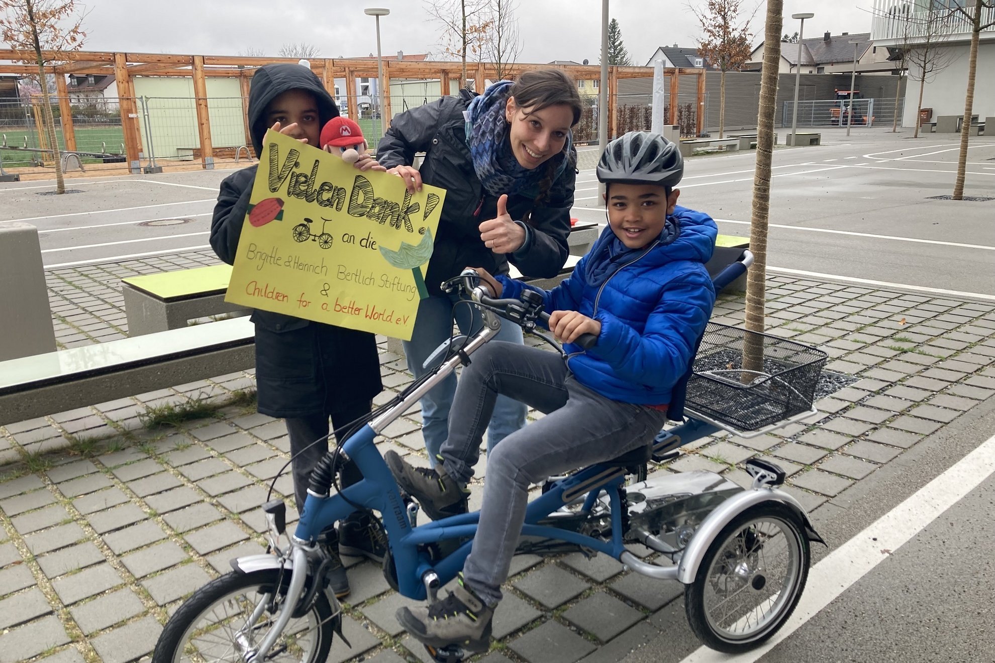Zwei Schüler und eine Lehrerin halten beim Verkehrsunterricht ein Plakat in den Händen, auf dem sie sich für die Spenden bedanken
