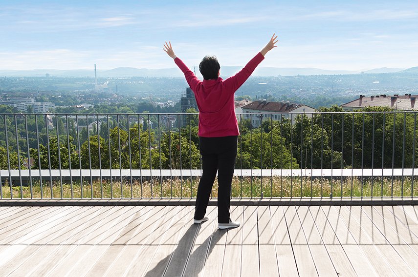Frau mit ausgebreiteten Armen auf einer Dachterrase