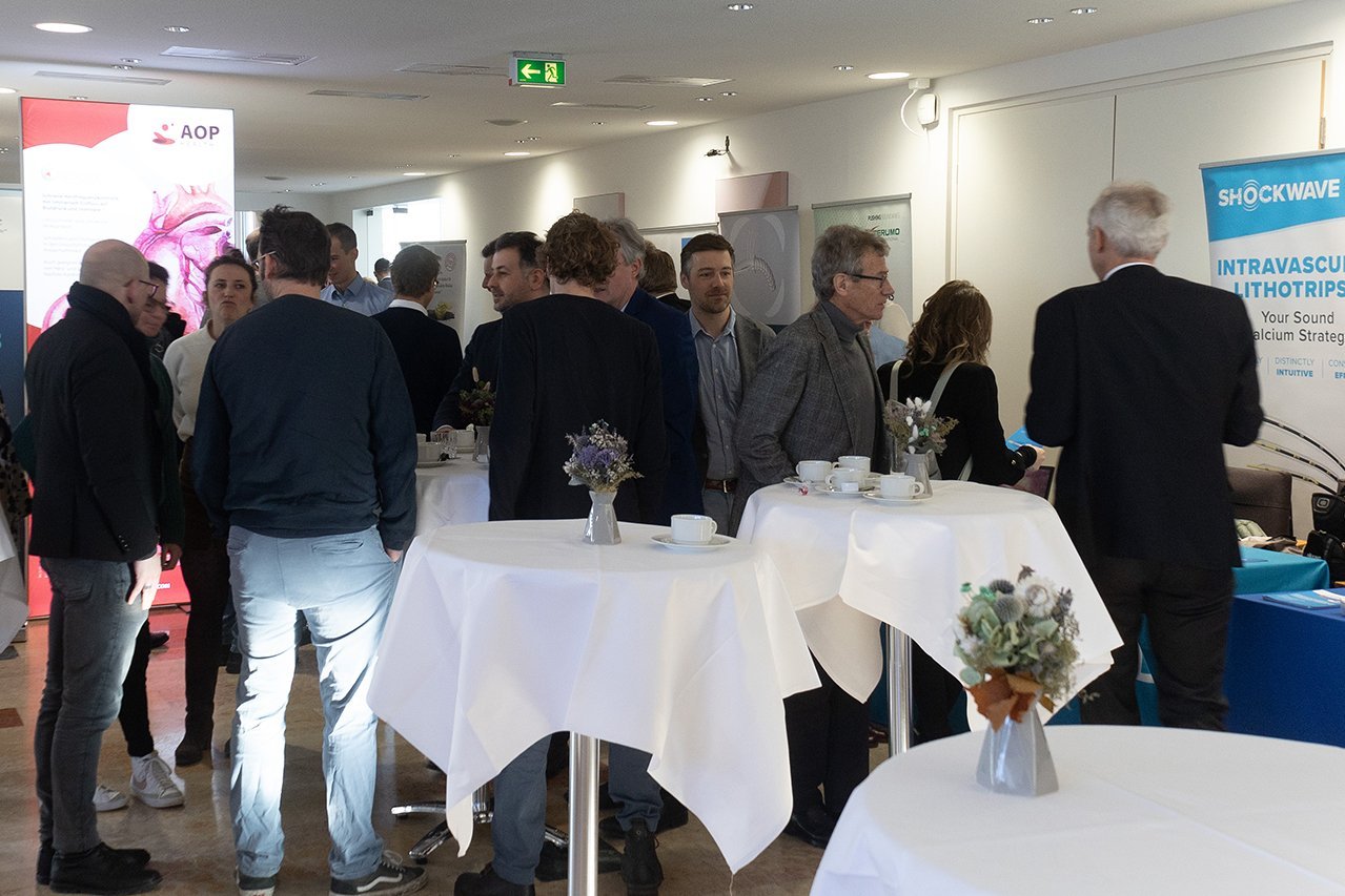 Besucher*innen bei der Industrieausstellung mit kleinen Tischen und Aufstellern zu verschiedenen Unternehmen im Rahmen des Symposiums