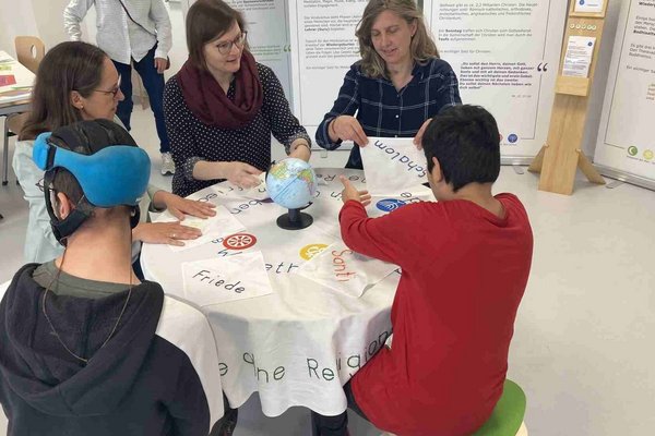 Drei Erwachsene und zwei Schüler sitzen gemeinsam an einem Tisch und beschäftigen sich mit den Weltreligionen