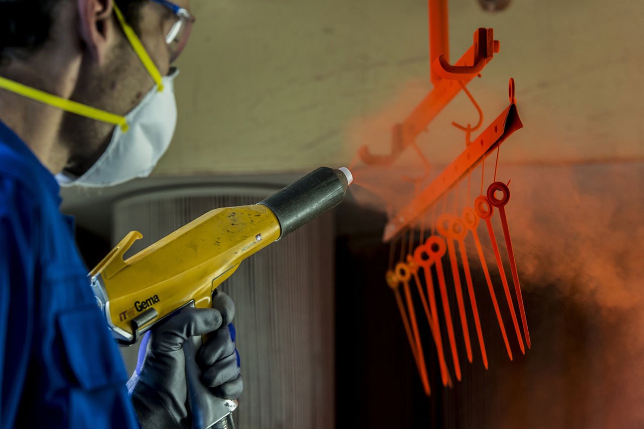 Ein Mann bespritzt ein Metallteil mit einer Pulverbeschichtungspistole
