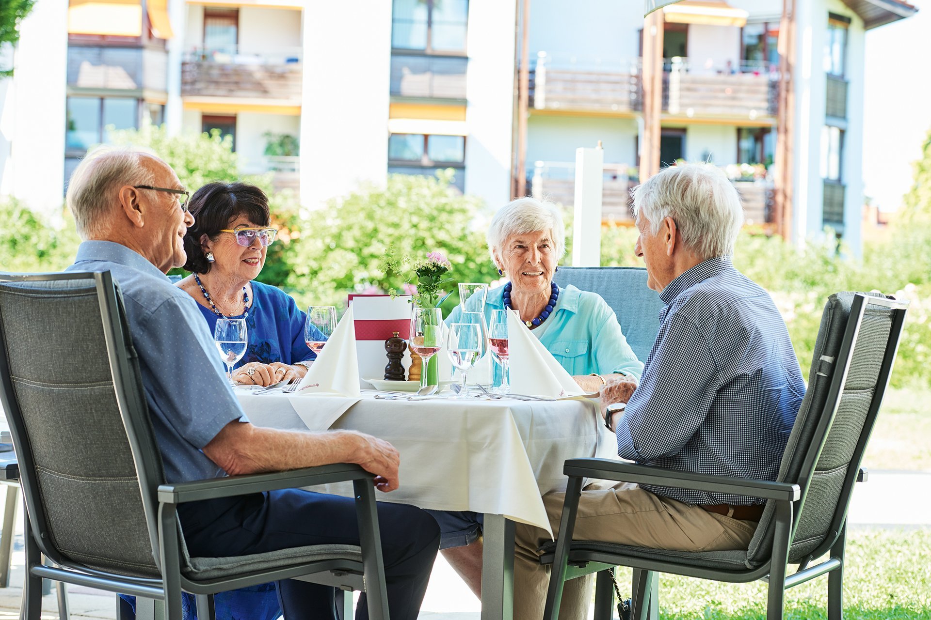 Vier Senior*innen sitzen an einem Tisch des Restaurants auf der Terrasse 