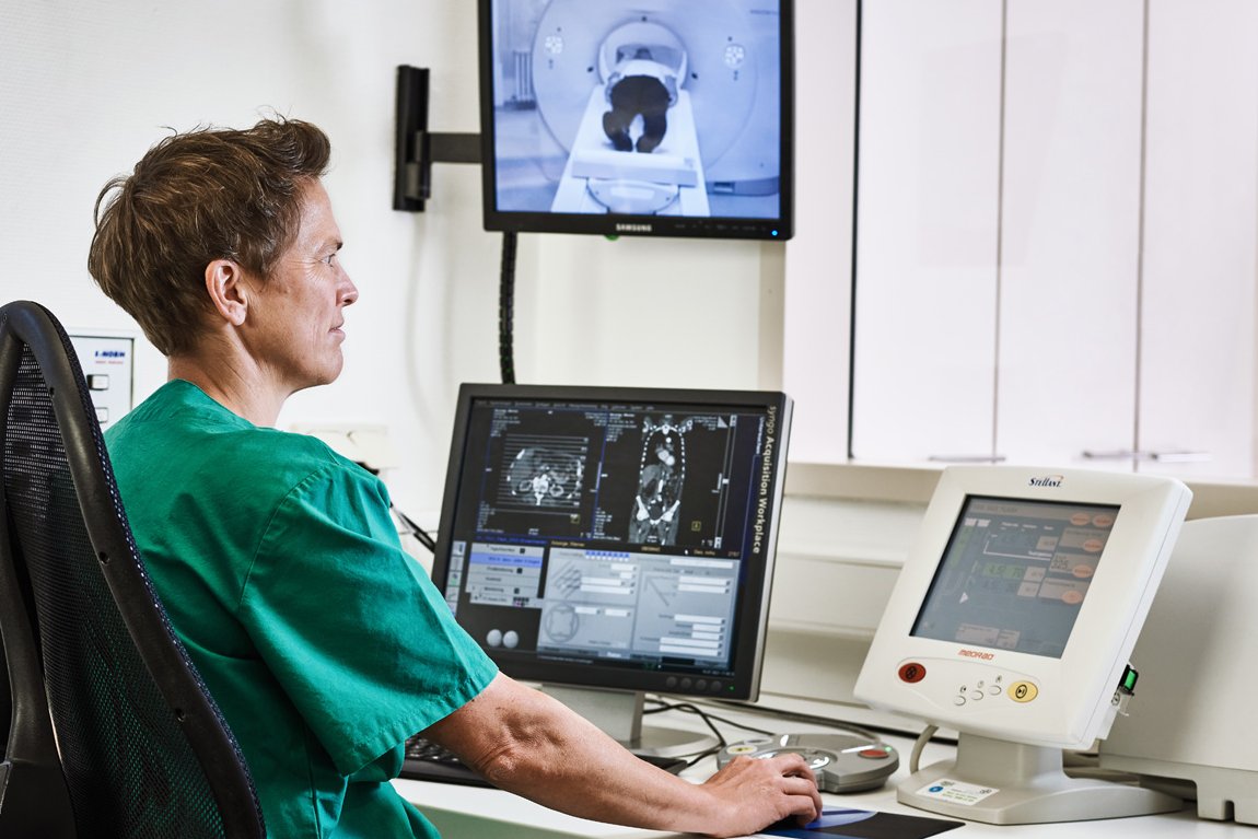 Eine Mitarbeiterin der Augustinum Klinik kontrolliert vor mehreren Bildschirmen sitzend eine Computertomographie