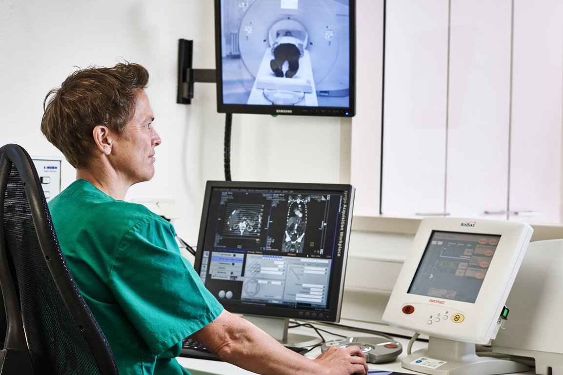 Eine Mitarbeiterin der Augustinum Klinik kontrolliert vor mehreren Bildschirmen sitzend eine Computertomographie