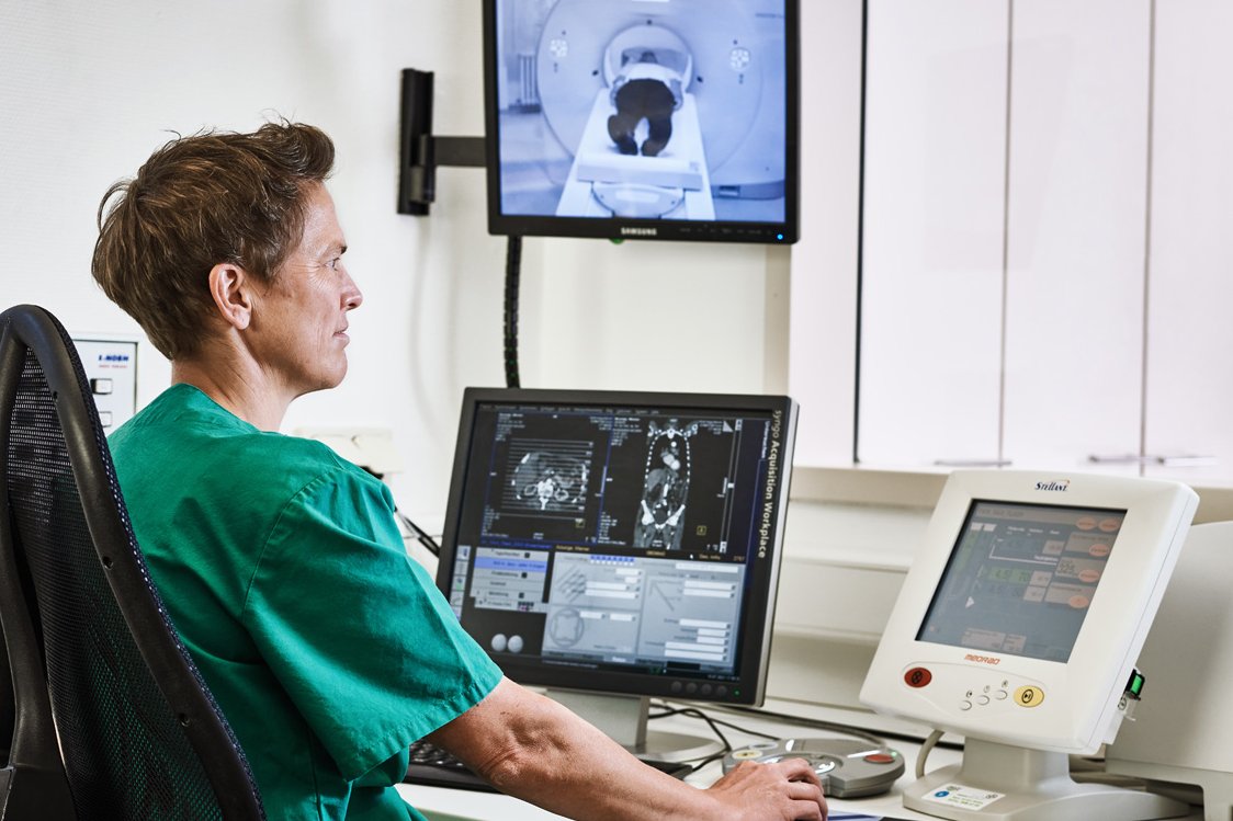 Eine Mitarbeiterin der Augustinum Klinik kontrolliert vor mehreren Bildschirmen sitzend eine Computertomographie