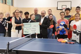 Ein Gruppenfoto mit Schüler*innen der Otto-Steiner-Schule hinter einer Tischtennisplatte mit einem Spendenscheck für die Tischtennisausstattung der Schule