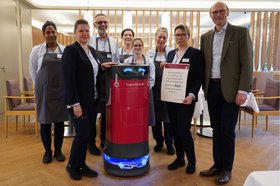 Service-Mitarbeiter*innen und der Geschäftsführer des Augustinum Kassel überreichen dem Abräum-Roboter eine Urkunde