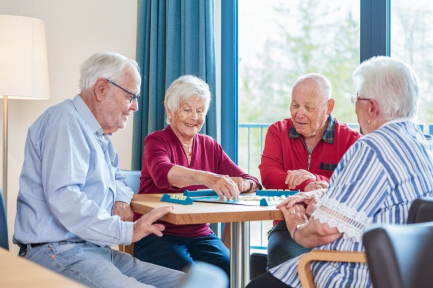 Vier Senior*inne sitzen gemeinsam an einem Tisch und spielen ein Gesellschaftsspiel