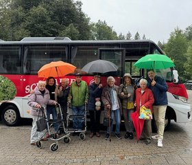 Senior*innen und Mitarbeiter*innen des Augustinum Berchtesgadener Land stehen mit Regenschirmen vor einem Kleinbus