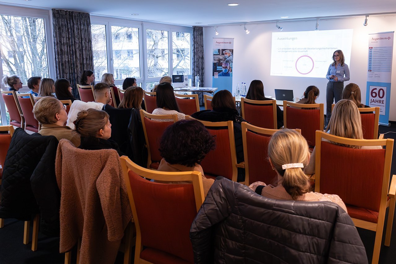 Die besetzten Stühle bei einem Workshop von hinten, wobei die Teilnehmer*innen auf Julia Niehaus schauen, die vor ihnen einen Vortrag hält 