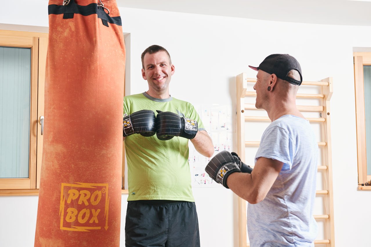 Zwei Bewohner stehen vor einem Boxsack, beide tragen Boxhandschuhe