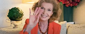 Eine Seniorin lächelt und winkt in die Kamera